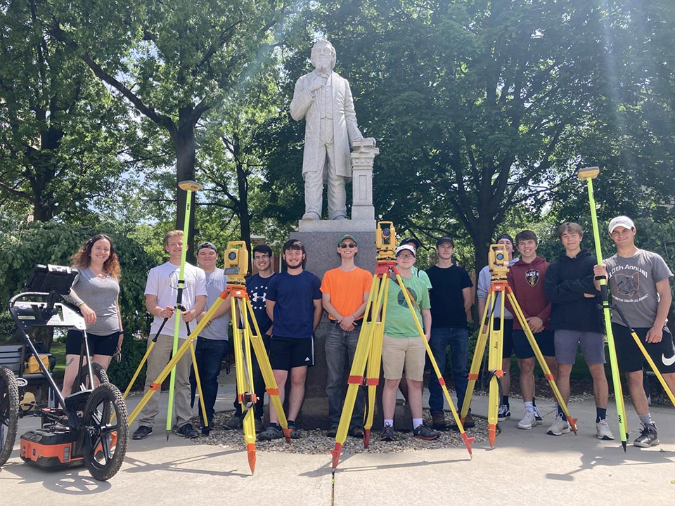University of Akron students standing in front of statue with surveying devices