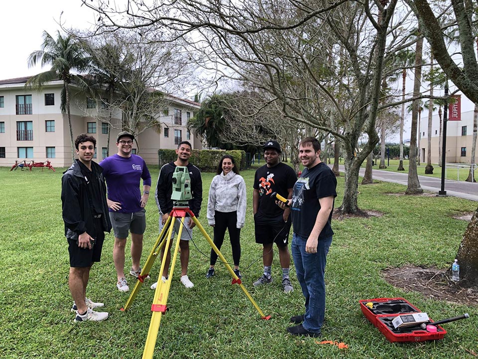 FAU students standing on campus with their survey tools