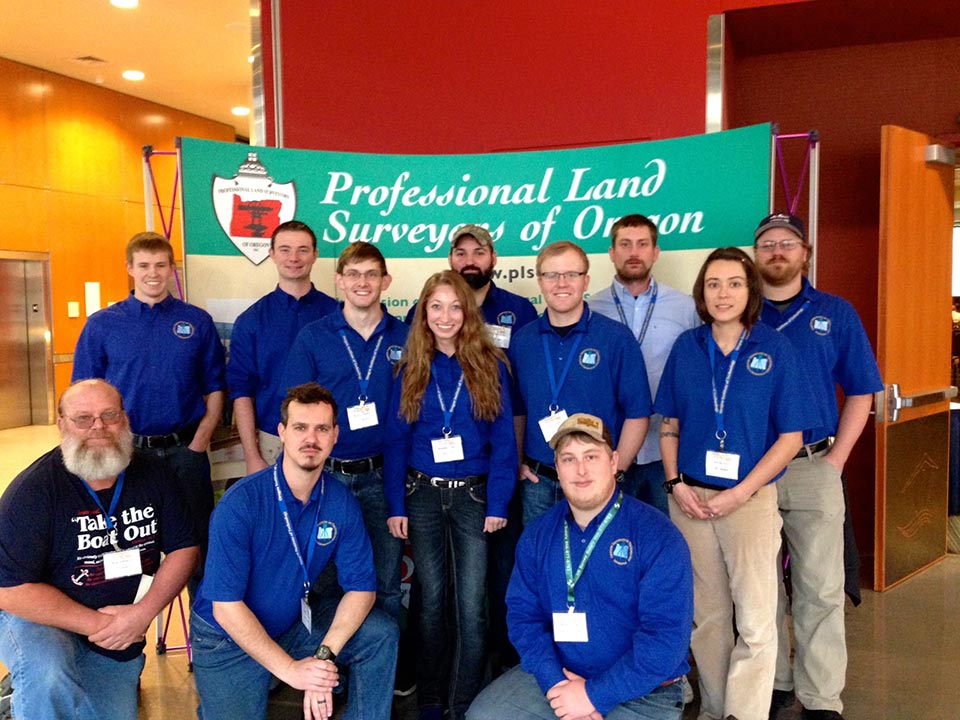 Students in blue standing in front of Professional Land Surveyors of Oregon sign