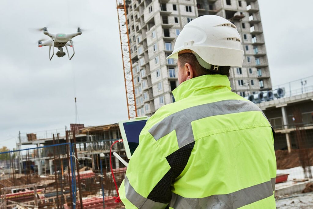 Hardhat and utility jacket worker flying a drone around buildings being built